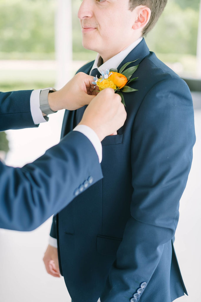 Handsome groom wearing a navy blue suit with a yellow flower perfect for a summer wedding by Christina Elliot Photography in Texas. how to dress your groom best suit for groom colors for groom to wear for summer wedding navy suit for groom yellow flowers for summer farmhouse wedding handsome groom for wedding #texasweddingphotographer #farmhousewedding #farmhouseweddinginspo #texasphotographer #farmhouseweddingdecor #texasweddinglocations