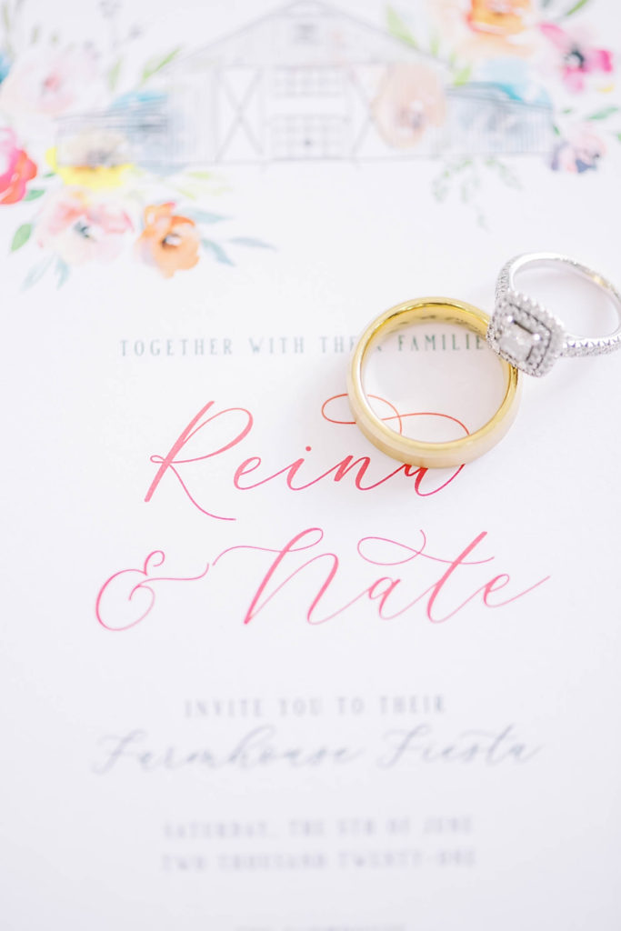 Classic wedding rings with pink flowers on invitations showing the perfect colors to use for a summer farmhouse wedding in Texas by Christina Elliot Photography. invitations for wedding pink flowers for wedding summer colors for farmhouse wedding perfect rings for him and her gold rings for groom texas wedding photographer how to plan your wedding texas wedding locations #texasweddingphotographer #farmhousewedding #farmhouseweddinginspo #texasphotographer #farmhouseweddingdecor #texasweddinglocations
