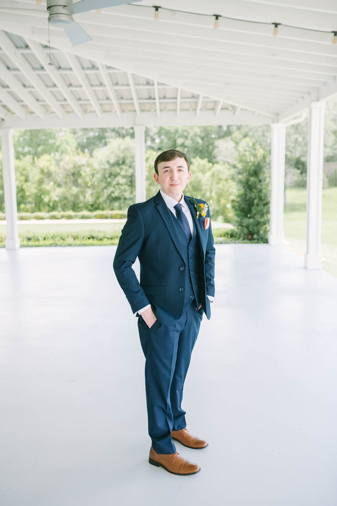 Christina Elliot Photography in Texas shows a handsome groom wearing a navy blue suit and brown shoes. how to dress your groom best suit for groom colors for groom to wear for summer wedding navy suit for groom yellow flowers for summer farmhouse wedding handsome groom for wedding blue suits for groom dressing your groom #texasweddingphotographer #farmhousewedding #farmhouseweddinginspo #texasphotographer #farmhouseweddingdecor #texasweddinglocations