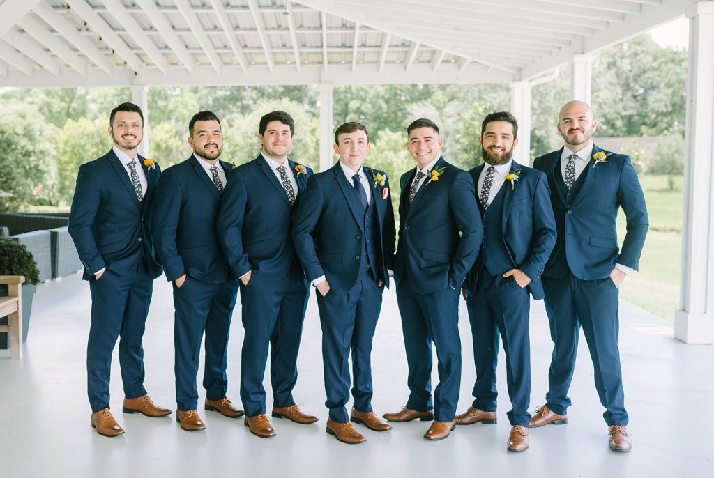 Handsome groom and groomsmen wearing a navy blue suit a yellow flower perfect for a summer wedding by Christina Elliot Photography in Texas. how to dress your groom best suit for groom colors for groom to wear for summer wedding navy suit for groom yellow flowers for summer farmhouse wedding handsome groom for wedding #texasweddingphotographer #farmhousewedding #farmhouseweddinginspo #texasphotographer #farmhouseweddingdecor #texasweddinglocations