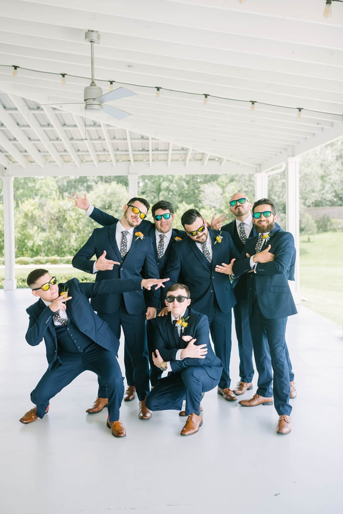 Christina Elliott Photography in Texas does a fun candid groomsmen photo at a summer farmhouse wedding. candid photos for bridal party how to photograph wedding party groomsmen outfits for wedding to wear for summer wedding navy suit for groom yellow flowers for summer farmhouse wedding handsome groom for wedding #texasweddingphotographer #farmhousewedding #farmhouseweddinginspo #texasphotographer #farmhouseweddingdecor #texasweddinglocations