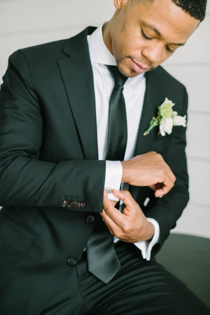 Groom does up his cuff link before his wedding wearing a black suit and tie by Christina Elliott Photography at The Farmhouse Montgomery. groom getting ready black suit and tie for wedding cuff link #christinaelliottphotography #christinaelliottweddings #TheFarmhouseMontgomery #farmhouseweddings #texasweddings #houstonweddingphotographers #mrandmrs #tildeathdowepart #weddingphotography #tietheknot #Houstonweddings #weddinginspiration #bride #groom