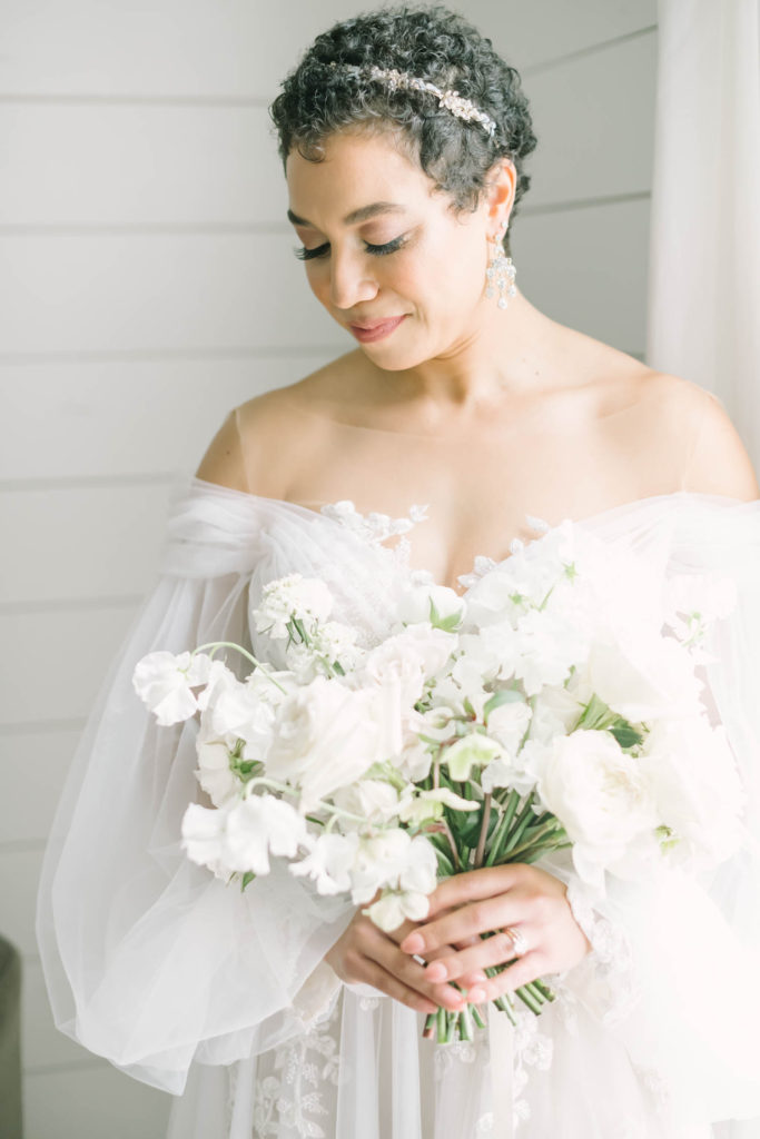 Christina Elliott Photography captures a photo of the bride with a diamond headband in her hair and flowy off-the-shoulder dress looking down in Houston, Texas. puffy sleeve wedding gown diamond headband short hair wedding style #christinaelliottphotography #christinaelliottweddings #TheFarmhouseMontgomery #farmhouseweddings #texasweddings #houstonweddingphotographers #mrandmrs #tildeathdowepart #weddingphotography #tietheknot #Houstonweddings #weddinginspiration #bride #groom
