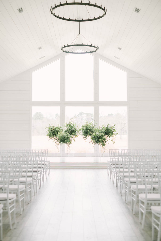 At The Farmhouse Montgomery in Houston, Texas the inside is white with big beautiful windows and a green plant altar, taken by Christina Elliott Photography. inside a farmhouse wedding set up wedding ideas white wedding location #christinaelliottphotography #christinaelliottweddings #TheFarmhouseMontgomery #farmhouseweddings #texasweddings #houstonweddingphotographers #mrandmrs #tildeathdowepart #weddingphotography #tietheknot #Houstonweddings #weddinginspiration #bride #groom