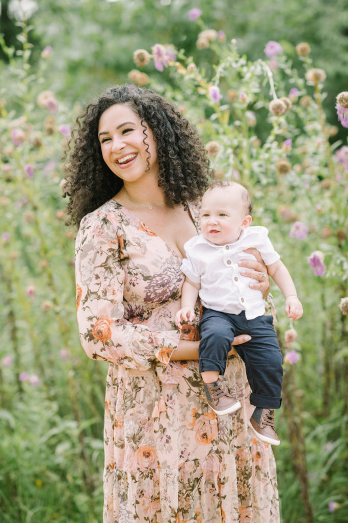 At the Houston Arboretum a mother holds her toddler little boy with navy pants and white button up in front of wild purple flowers by Christina Elliott Photography. happy mother with baby boy purple wildflowers #christinaelliottphotography #christinaelliottfamilies #houstonfamilyphotographer #familyofthree #Houstonarboretum #babyboy #familypictures #outdoorfamilypictures #summerfamilypics #familyphotos #famiyphotographer #Houstonfamilyphotos