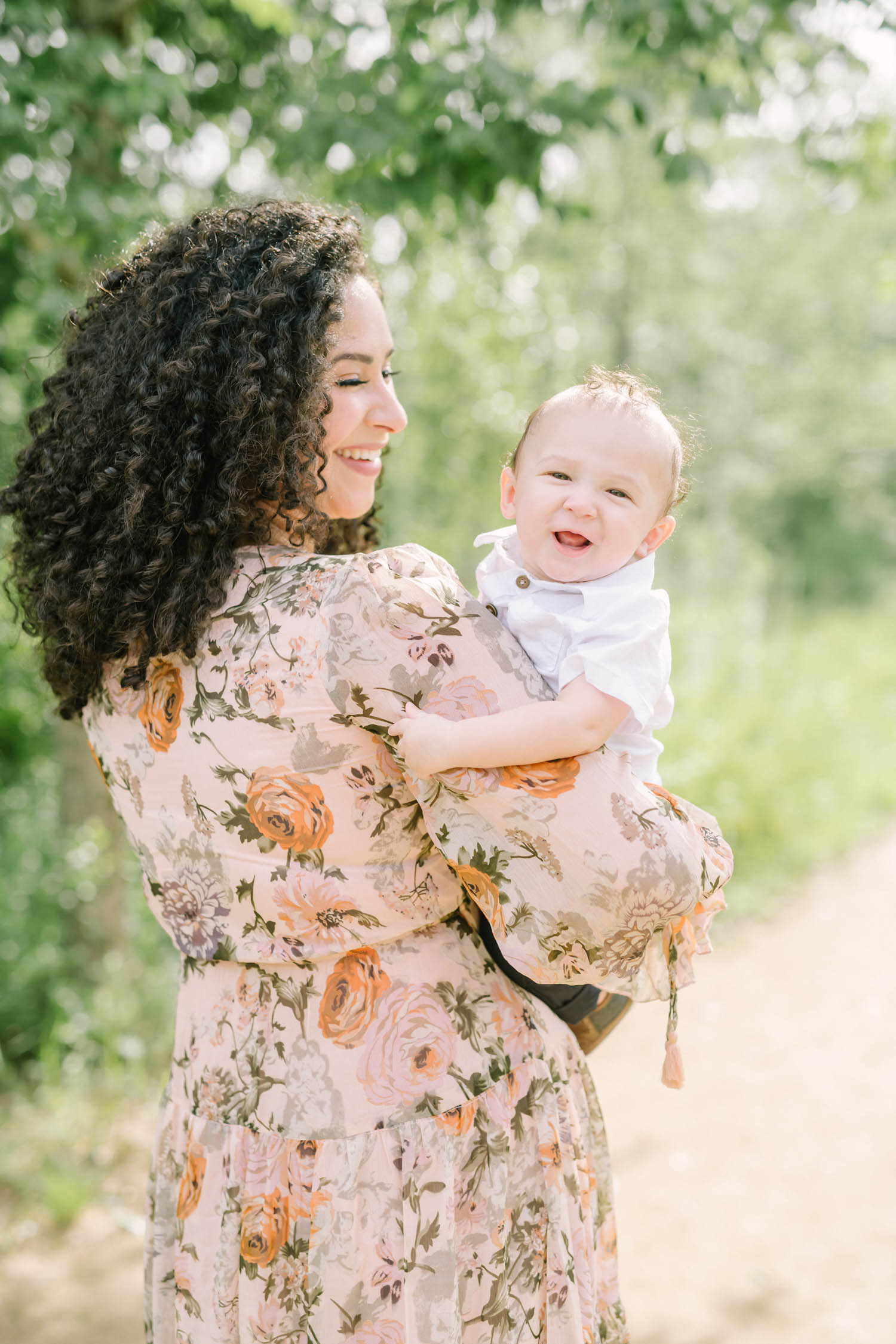 A darling photo of a mother smiling at her baby boy as he smiles over her shoulder at the Houston Arboretum by Christina Elliott Photography. mother and child mother's love happy smiling baby baby under the age of one in family pictures #christinaelliottphotography #christinaelliottfamilies #houstonfamilyphotographer #familyofthree #Houstonarboretum #babyboy #familypictures #outdoorfamilypictures #summerfamilypics #familyphotos #famiyphotographer #Houstonfamilyphotos