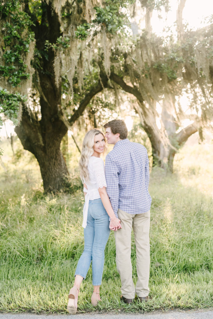 In Houston, a darling couple holds hands and looks back as the sun shines through mossy trees behind them by Christina Elliott Photography, a professional couple photographer. darling engagement poses sunlight through trees #christinaelliottphotography #christinaelliottengagements #houstonengagements #brazosbendstateparkengagements #brazosbendphotography #houstonengagementphotographer #weddingannoucementphotos #houstonphotographers #couplegoals #soontobemarried #engaged #engagementphotos