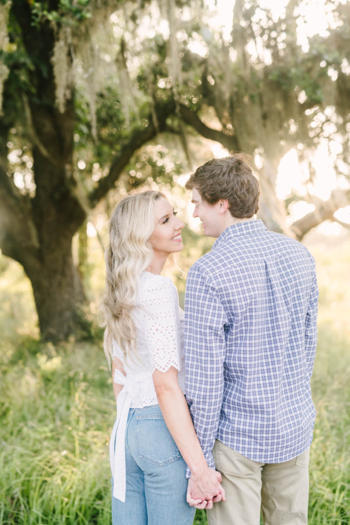 A woman in a white eyelet blouse smiles at a man in a blue plaid button-up shirt at Brazos Bend State Park with engagement photographer Christina Elliott Photography. casual engagement outfits white eyelet top button-up shirt #christinaelliottphotography #christinaelliottengagements #houstonengagements #brazosbendstateparkengagements #brazosbendphotography #houstonengagementphotographer #weddingannoucementphotos #houstonphotographers #couplegoals #soontobemarried #engaged #engagementphotos
