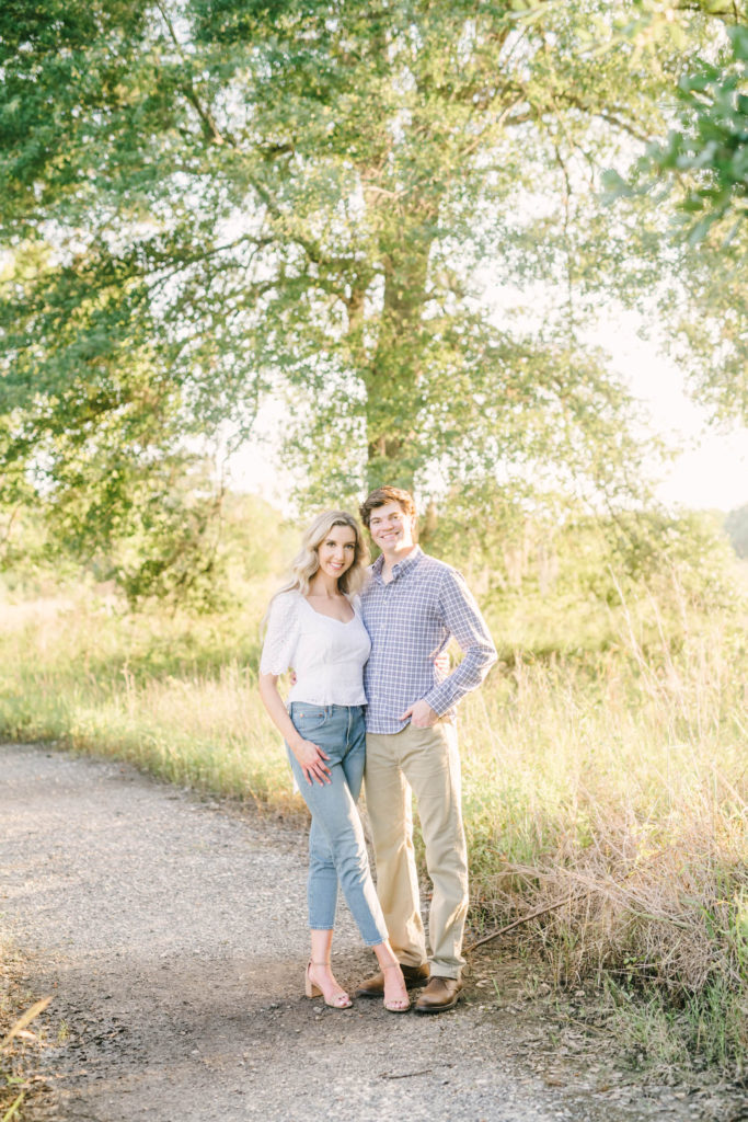 Christina Elliott Photography captures a couple standing together and smiling for a portrait on a dirt path in a Texas State Park. dirt path portraits sunset photography couple portrait ideas #christinaelliottphotography #christinaelliottengagements #houstonengagements #brazosbendstateparkengagements #brazosbendphotography #houstonengagementphotographer #weddingannoucementphotos #houstonphotographers #couplegoals #soontobemarried #engaged #engagementphotos
