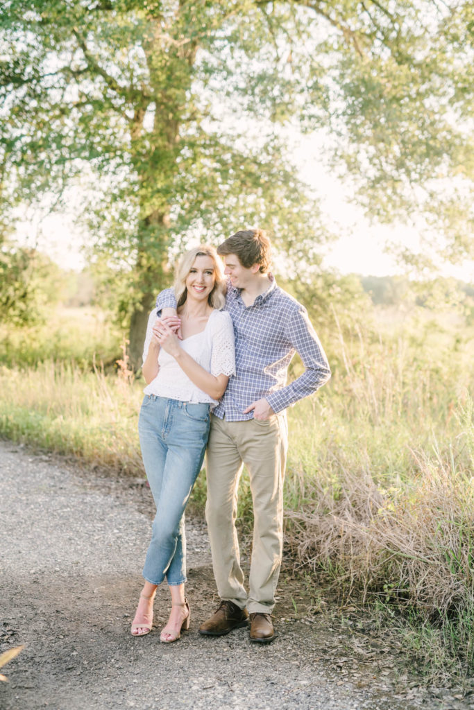 A man in tan pants and blue button-up shirt puts his arm around his fiance and smiles lovingly at her during sunset at Brazos Bend State Park in Houston by Christina Elliott Photography. couple goals engaged engagements #christinaelliottphotography #christinaelliottengagements #houstonengagements #brazosbendstateparkengagements #brazosbendphotography #houstonengagementphotographer #weddingannoucementphotos #houstonphotographers #couplegoals #soontobemarried #engaged #engagementphotos