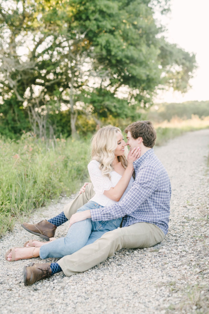 A bride-to-be sits in between her groom's legs on a gravel path and goes in for a kiss at Brazos Bend State Park by Christina Elliott Photography. couple poses intimate couple poses Houston wedding photographers #christinaelliottphotography #christinaelliottengagements #houstonengagements #brazosbendstateparkengagements #brazosbendphotography #houstonengagementphotographer #weddingannoucementphotos #houstonphotographers #couplegoals #soontobemarried #engaged #engagementphotos