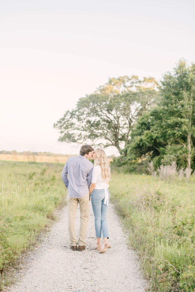 Houston Wedding Photographer Christina Elliott Photography captures a newly engaged couple kissing on a gravel dirt path with green wild grass to the side in Houston. Kissing poses newly engaged cute engaged photos #christinaelliottphotography #christinaelliottengagements #houstonengagements #brazosbendstateparkengagements #brazosbendphotography #houstonengagementphotographer #weddingannoucementphotos #houstonphotographers #couplegoals #soontobemarried #engaged #engagementphotos