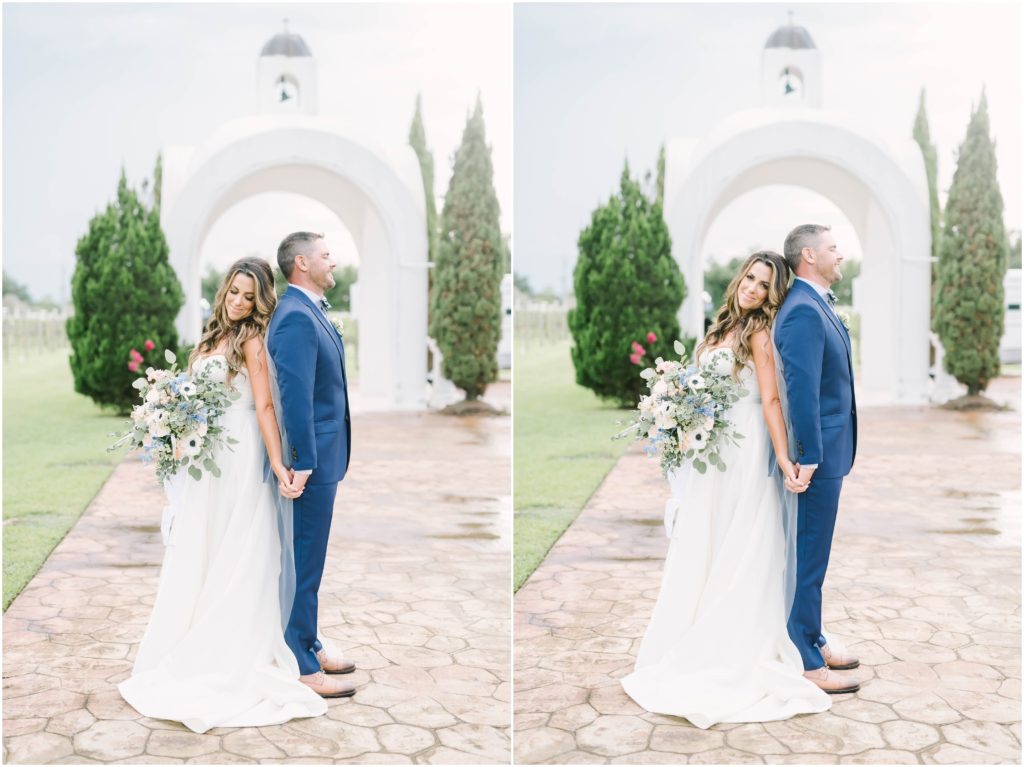 Bride and groom stand back to back while holding hands in front of a beautiful arch bell tower at a Winery in Houston captured by Christina Elliott Photography. bride and groom back to back newly wed pose ideas wedding inspiration #christinaelliottphotography #christinaelliottweddings #Winerywedding #Houstonweddings #newlyweds #weddingdress #weddingphotography #Houstonweddingphotographers #dreamyweddings #bluesuit #weddingstyle #mrandmrs #weddinggoals #Houstonphotographers