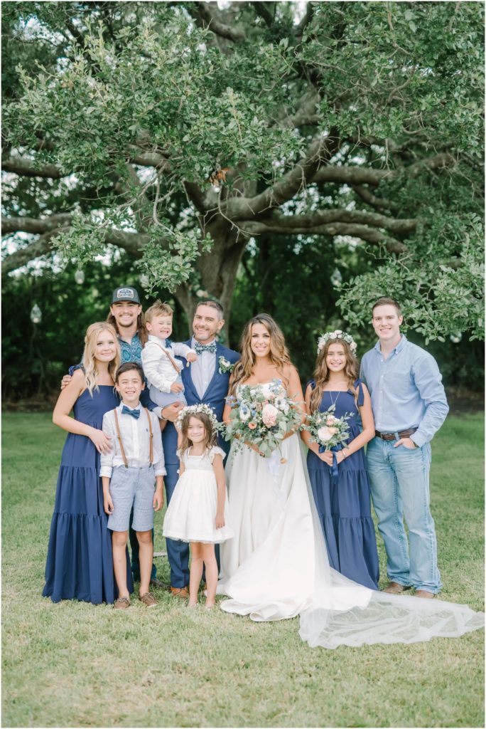 Bride and groom take family picture with all their children wearing blues and white by Houston photographer Christina Elliott Photography. wedding with all the kids family picture at wedding yours mine and ours wedding #christinaelliottphotography #christinaelliottweddings #Winerywedding #Houstonweddings #newlyweds #weddingdress #weddingphotography #Houstonweddingphotographers #dreamyweddings #bluesuit #weddingstyle #mrandmrs #weddinggoals #Houstonphotographers
