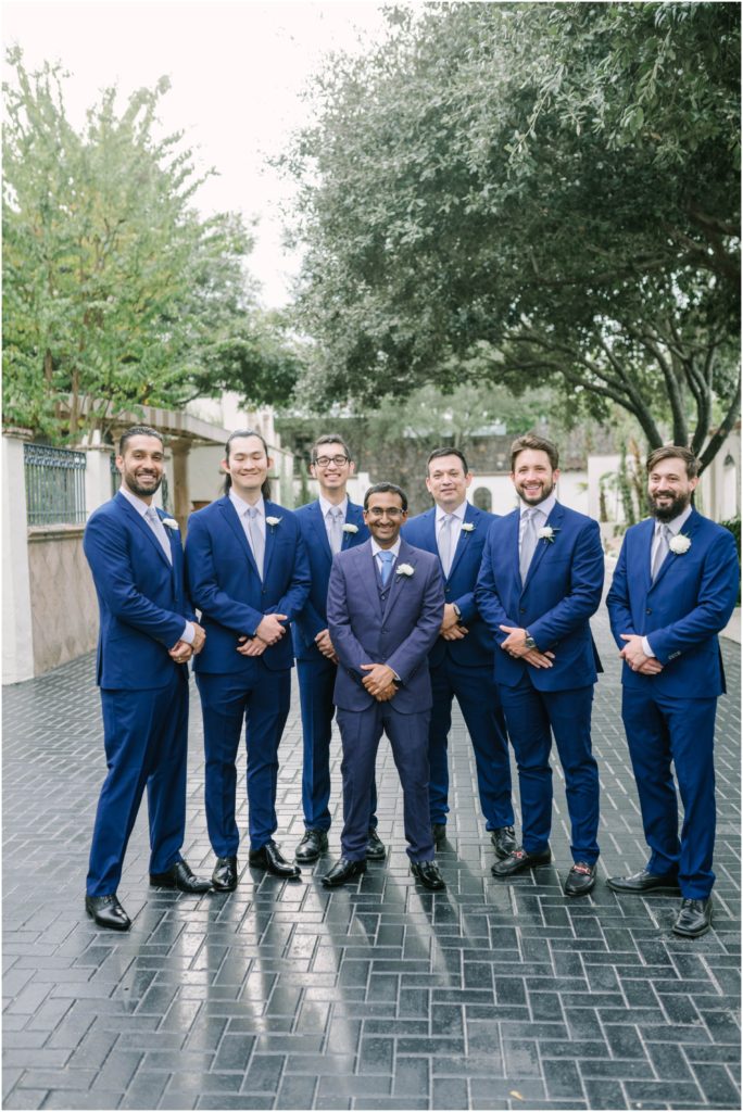 Groomsmen in cobalt blue suits and light blue ties surround the groom who is the shortest in the middle by Christina Elliott Photography of the Houston area. Houston weddings groomsmen in blue blue suit black shoes #christinaelliottphotography #christinaelliottweddings #thebelltoweron34th #belltowerwedding #houstonweddings #houstonweddingphotographers #mrandmrs #newlymarried #weddinginspiration #bridalgown #groomstyle #texasweddingphotographers #tietheknot #traditionalindianwedding