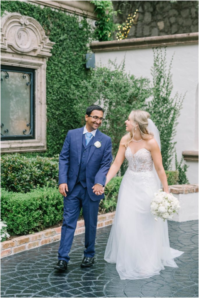 A newly married couple look into one another's eyes and laugh while walking through a beautiful courtyard in Houston by Christina Elliott Photography. laughing newly weds courtyard weddings #christinaelliottphotography #christinaelliottweddings #thebelltoweron34th #belltowerwedding #houstonweddings #houstonweddingphotographers #mrandmrs #newlymarried #weddinginspiration #bridalgown #groomstyle #texasweddingphotographers #tietheknot #traditionalindianwedding