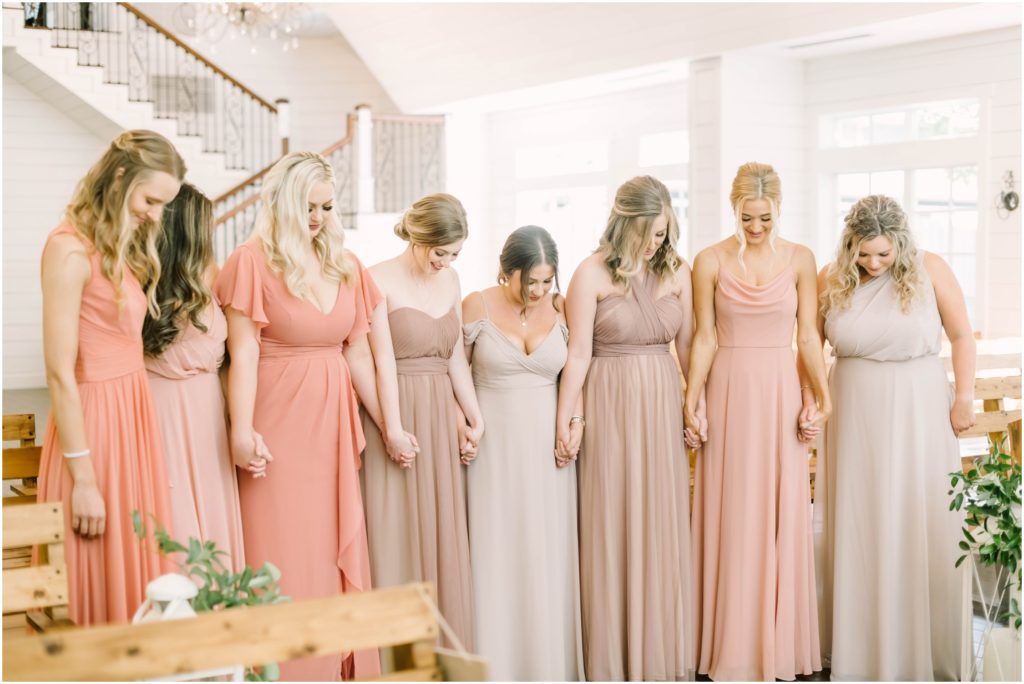 Bridesmaids all in shades of pinks hold hands and pray together before the wedding in Houston by Christina Elliott Photography. bridesmaids in pinks bridesmaids dresses prayer for wedding #christinaelliottphotography #christinaelliottweddings #houstontx #houstonweddings #houstonweddingphotographers #carriagehousewedding #conroetexas #texasweddingvenues #carriagehousechapel #cottageweddings #farmhousewedding #sweatheartweddinggown #countrywedding #weddinginspiration