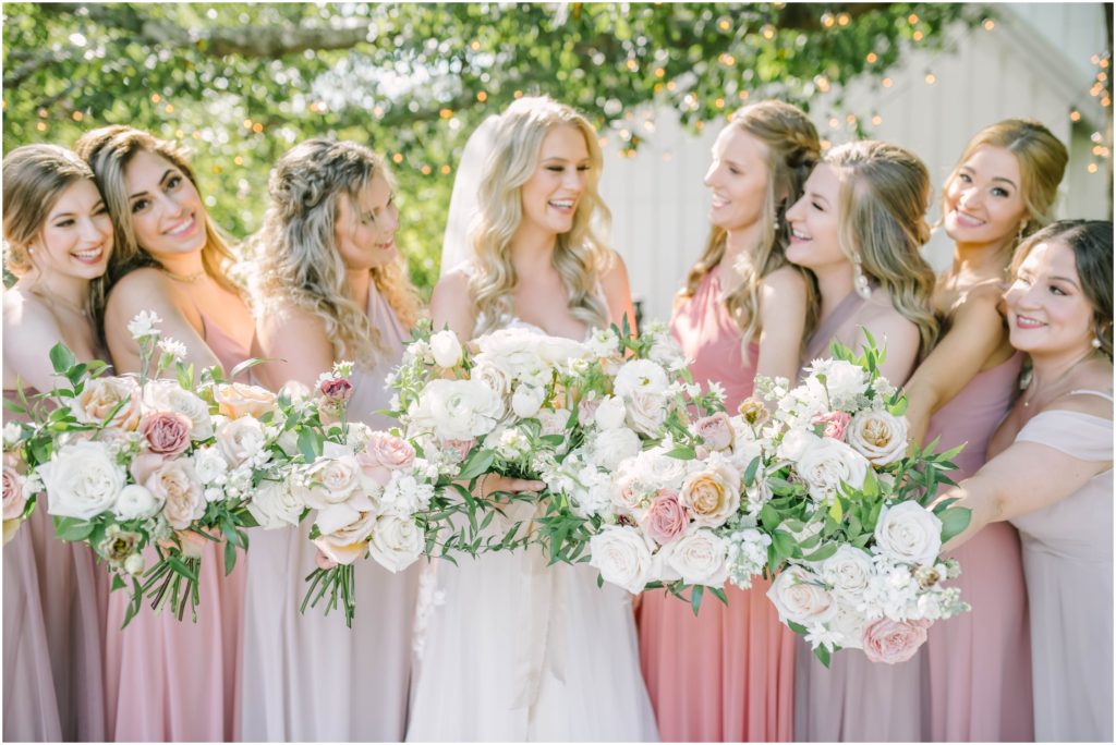 Christina Elliott Photography captures a portrait of the bridesmaids all smiling at the bride as they hold their bouquets forward near Houston, Texas. bridal party darling bridesmaids candid wedding party pic #christinaelliottphotography #christinaelliottweddings #houstontx #houstonweddings #houstonweddingphotographers #carriagehousewedding #conroetexas #texasweddingvenues #carriagehousechapel #cottageweddings #farmhousewedding #sweatheartweddinggown #countrywedding #weddinginspiration