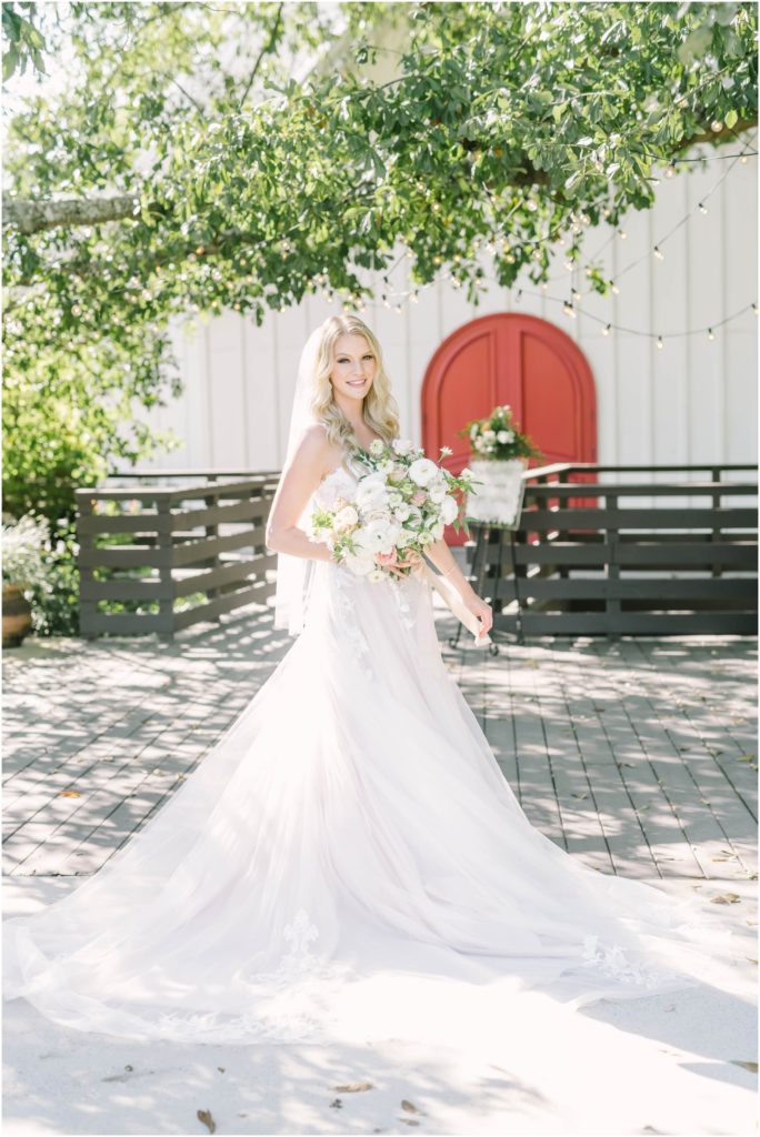 Bride with her wedding gown spread out in a fan smiles while holding her white and pink bouquet in Conroe, Texas by Christina Elliott Photography. bridal gown fan say yes to the dress bridal portrait #christinaelliottphotography #christinaelliottweddings #houstontx #houstonweddings #houstonweddingphotographers #carriagehousewedding #conroetexas #texasweddingvenues #carriagehousechapel #cottageweddings #farmhousewedding #sweatheartweddinggown #countrywedding #weddinginspiration
