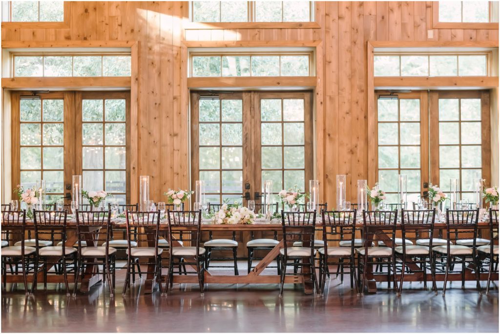 Wedding party table in a wooden barn with wood chairs and glass candle rings at The Carriage House by Christina Elliott Photography a Houston photographer. wedding party long table wedding luncheon in barn #christinaelliottphotography #christinaelliottweddings #houstontx #houstonweddings #houstonweddingphotographers #carriagehousewedding #conroetexas #texasweddingvenues #carriagehousechapel #cottageweddings #farmhousewedding #sweatheartweddinggown #countrywedding #weddinginspiration