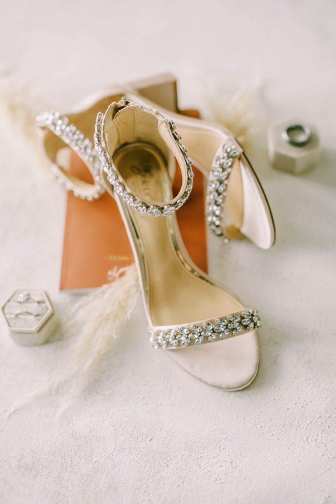 Jeweled bridal shoes stacked on a rust vow book and styled with pampas grass and a velvet ring box.