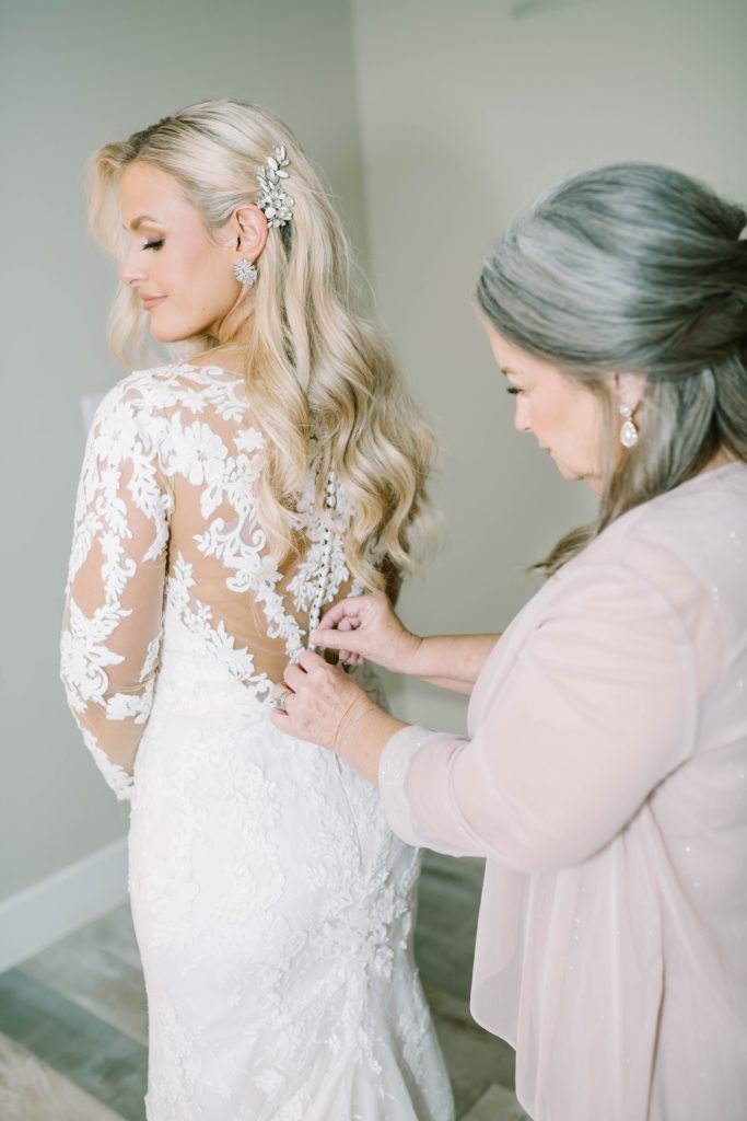 Mother of the bride buttons up her daughter's wedding dress at Still Waters Ranch in Texas by Christina Elliott Photography. mother of the bride helps get her ready #christinaelliottphotography #texasweddingphotographer #ranchwedding #countrychic