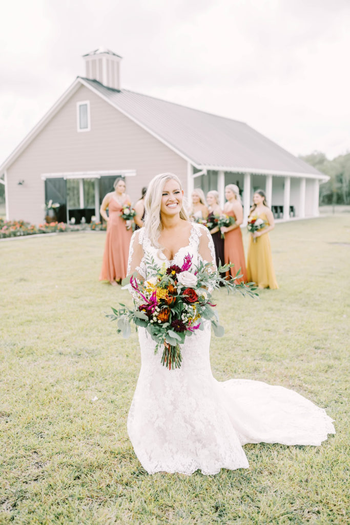 Standing in front of a barn in Texas a bride laughs as her bridesmaids stand behind her by Christina Elliott Photography. country chic bridesmaid style ideas #christinaelliottphotography #texasweddingphotographer #ranchwedding #countrychic