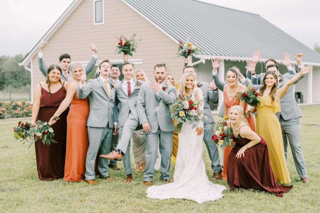 The bridal party celebrates throwing bouquets up and around the bride and groom in Texas by Christina Elliott Photography. bridal party shots gray suits for groomsmen #christinaelliottphotography #texasweddingphotographer #ranchwedding #countrychic