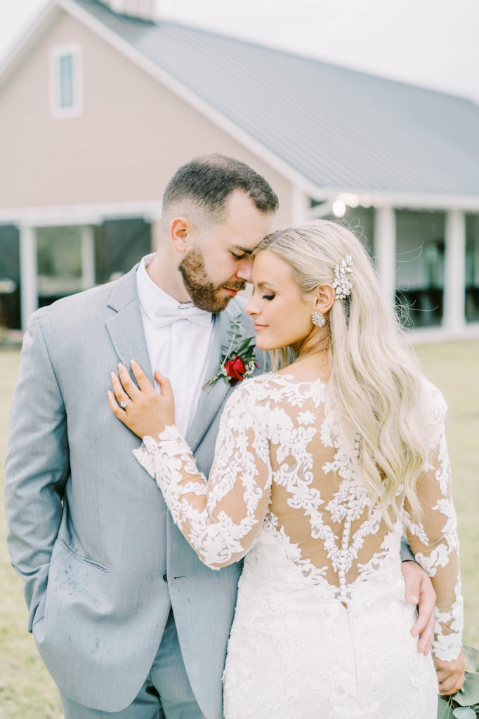 Sheer lace v back dress with little buttons down the lace and bride and groom holding each other by Christina Elliott Photography. lace dress back little white buttons #christinaelliottphotography #texasweddingphotographer #ranchwedding #countrychic
