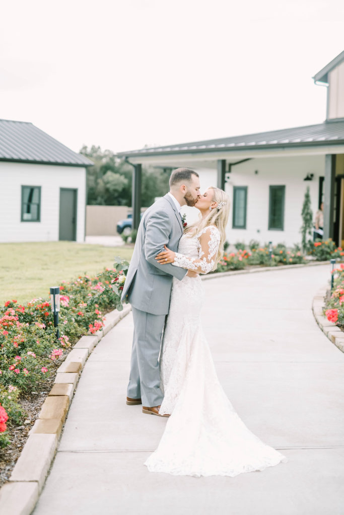 During a country Texas wedding a bride and groom kiss on a floral farm pathway by Christina Elliott Photography. country wedding venues country romantic chic wedding #christinaelliottphotography #texasweddingphotographer #ranchwedding #countrychic