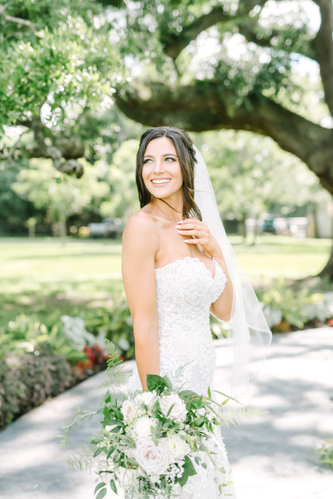 At Oak Plantation in Texas bride wearing a lace fitted gown and white rose bouquet smiles under the trees by Christina Elliott Photography. white rose bouquet #texasbridals #christinaelliottphotography #plantationwedding #bridalinspiration #TXwedding