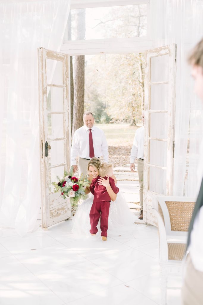 Christina Elliott Photography captures a mother bride hugging her little boy wearing a maroon suit. bride hugs son wedding in the Texas woods #christinaelliottphotography #theoakatelierwedding #Houstonwinterweddings #weddingphotographersHouston