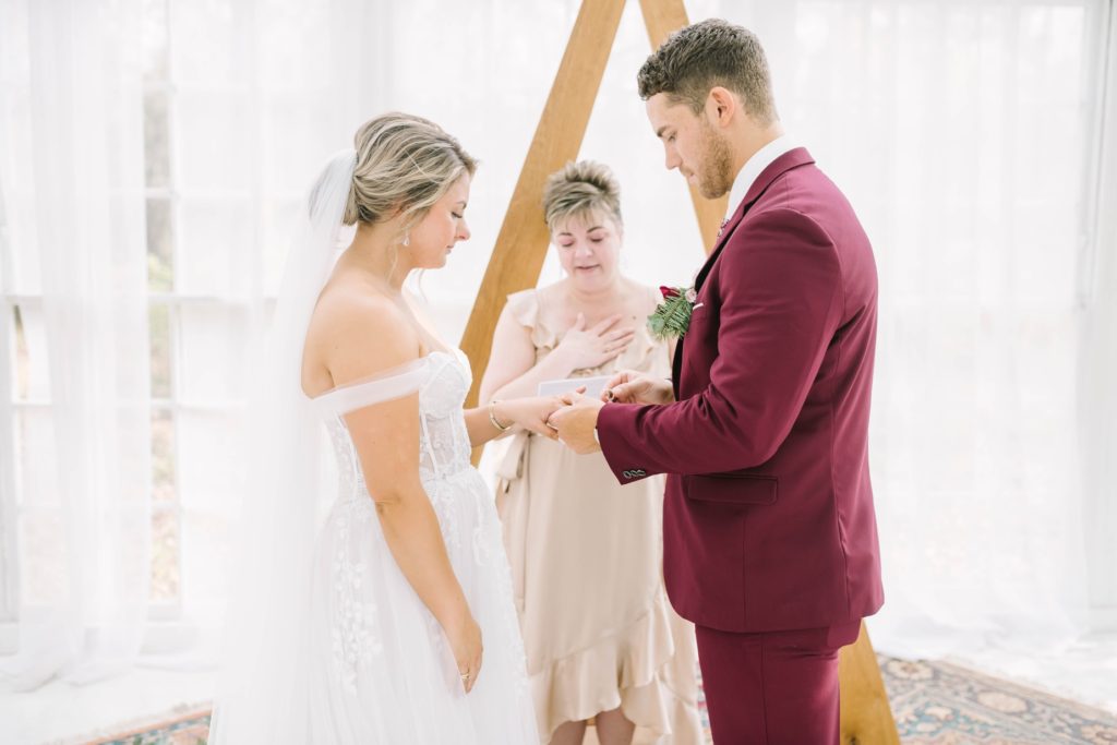 Groom puts the wedding ring on his bride's finger during a wedding ceremony by Christina Elliott Photography. wedding ceremony portraits in TX #christinaelliottphotography #theoakatelierwedding #Houstonwinterweddings #weddingphotographersHouston