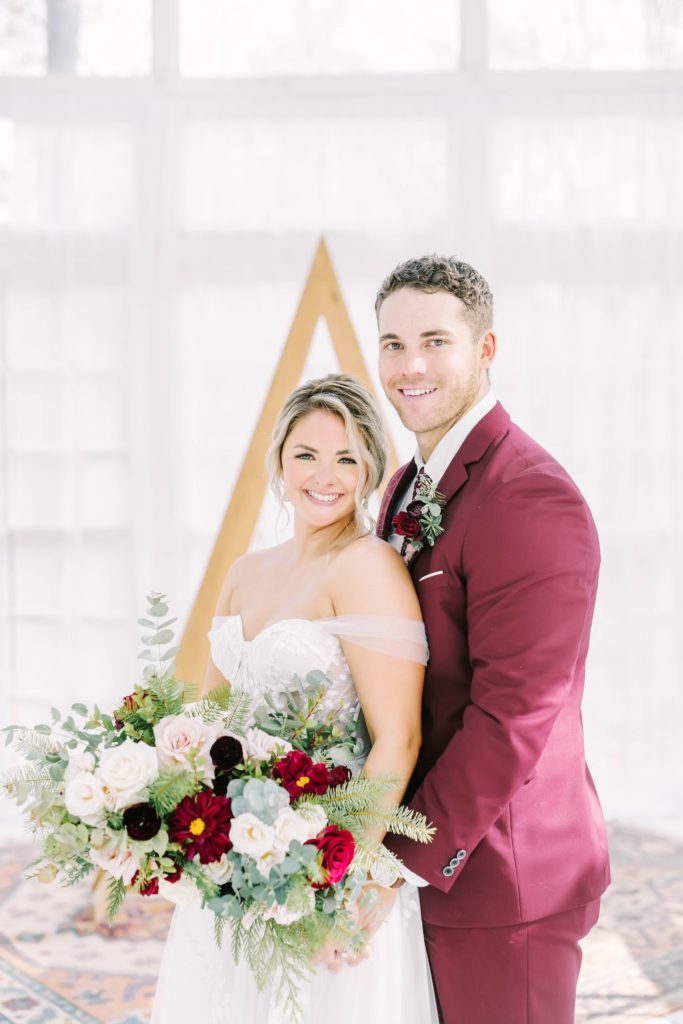 A maroon groom suit and winter wedding bouquet were captured by wedding photographer Christina Elliott Photography. unique wedding gowns winter #christinaelliottphotography #theoakatelierwedding #Houstonwinterweddings #weddingphotographersHouston