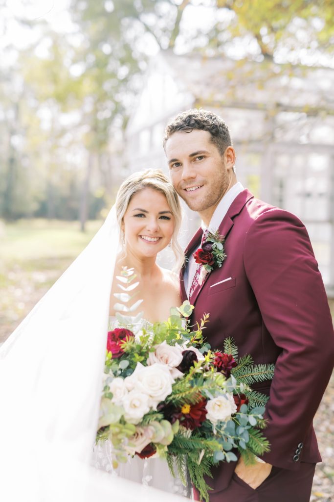 The newly married couple smiles with the sun shining in Houston, Texas by Christina Elliott Photography. bridal bouquet with pine branches #christinaelliottphotography #theoakatelierwedding #Houstonwinterweddings #weddingphotographersHouston