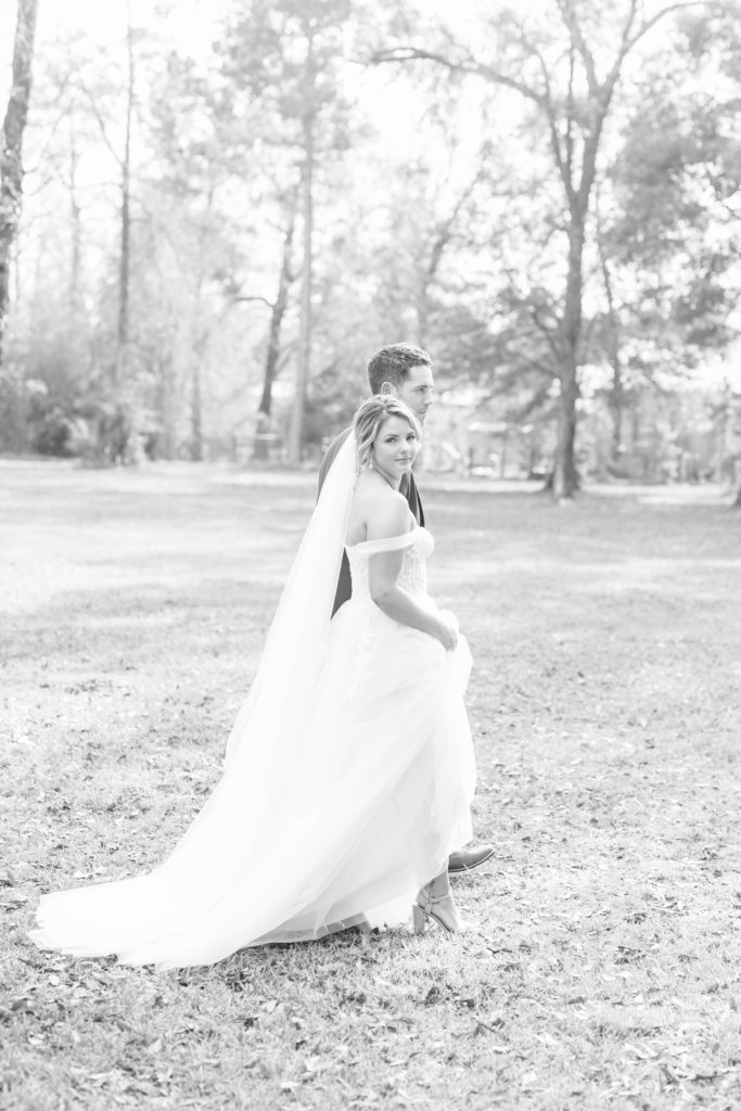 Black and white portrait of a newly married couple walking in a forest by Christina Elliott Photography. wedding black and white portrait #christinaelliottphotography #theoakatelierwedding #Houstonwinterweddings #weddingphotographersHouston