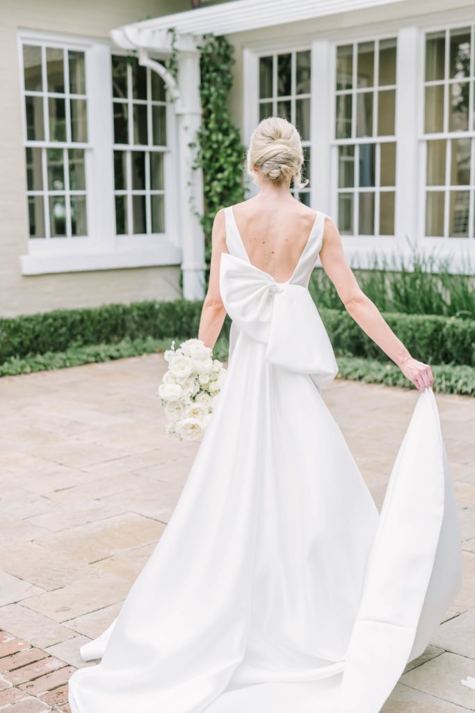 Large silk floppy bow on the back of a bridal gown captured by Christina Elliott Photography. silk floppy bow bridal updo ideas and inspirations #christinaelliottphotography #houstonweddings #riveroaksgardenclub #outdoorbridals #houstonbridals