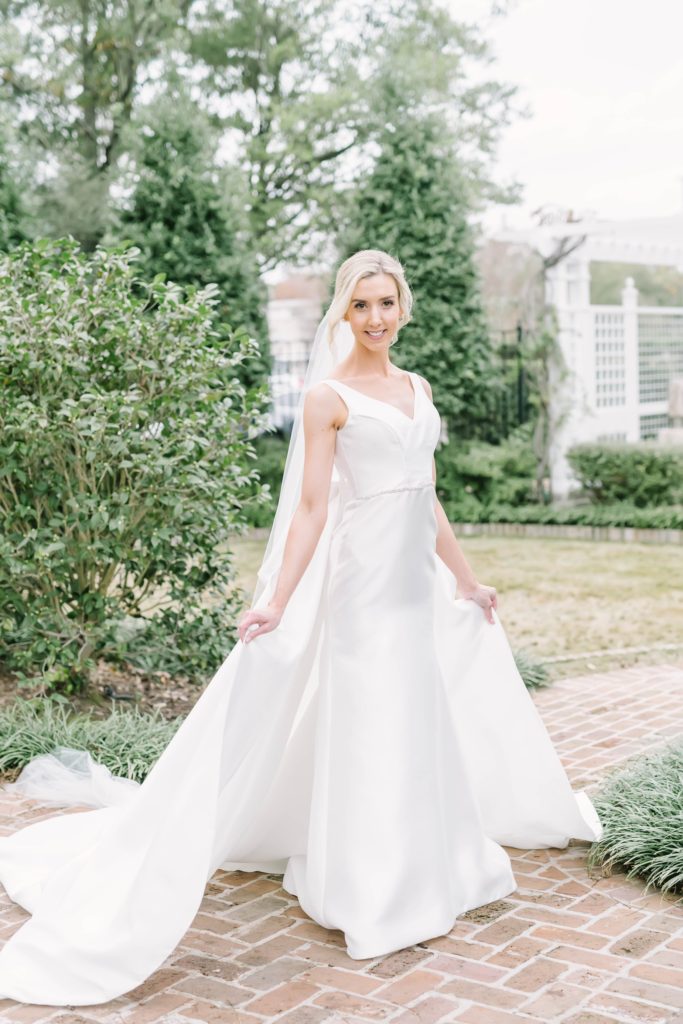 Blonde bride with traditional silk v neck wedding gown with full veil by Christina Elliott Photography. v neck wedding gown fitted wedding gown #christinaelliottphotography #houstonweddings #riveroaksgardenclub #outdoorbridals #houstonbridals