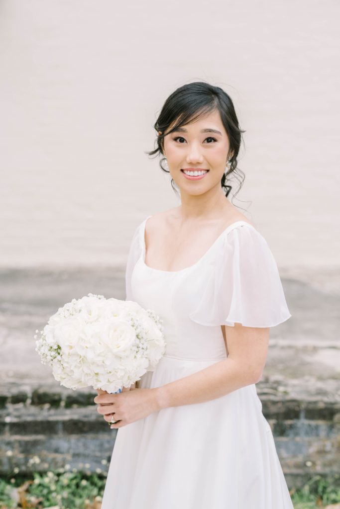 Bride with sheer flutter sleeve smiles in Houston for Christina Elliott Photography during her wedding. white floral wedding bouquet minimalist wedding gown #christinaelliottphotography #thesamhoustonhotel #houstonweddings #TXweddingphotographer