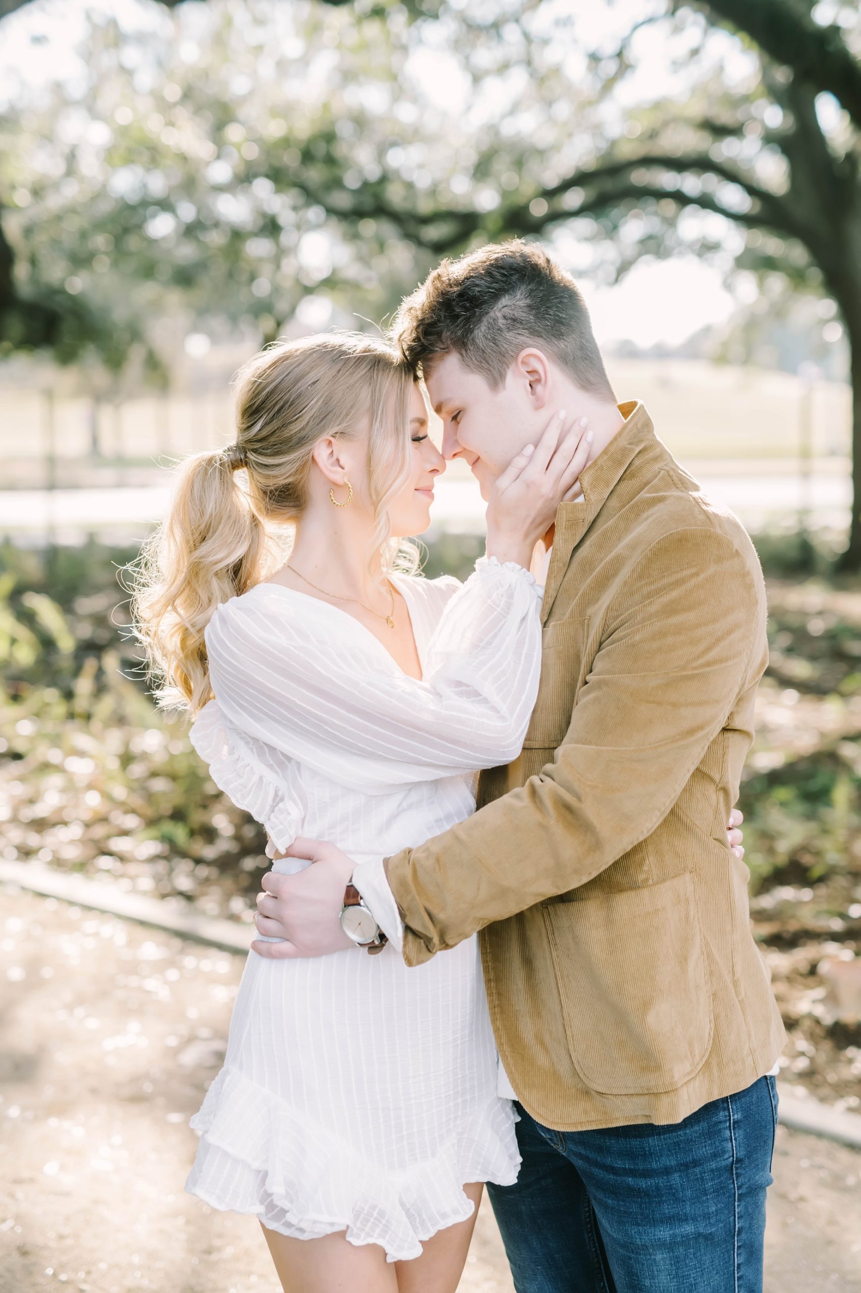 Couple snuggle their faces together, while bride with a blond ponytail holds her fiances face at McGovern Centennial Gardens. Houston Wedding Photography.