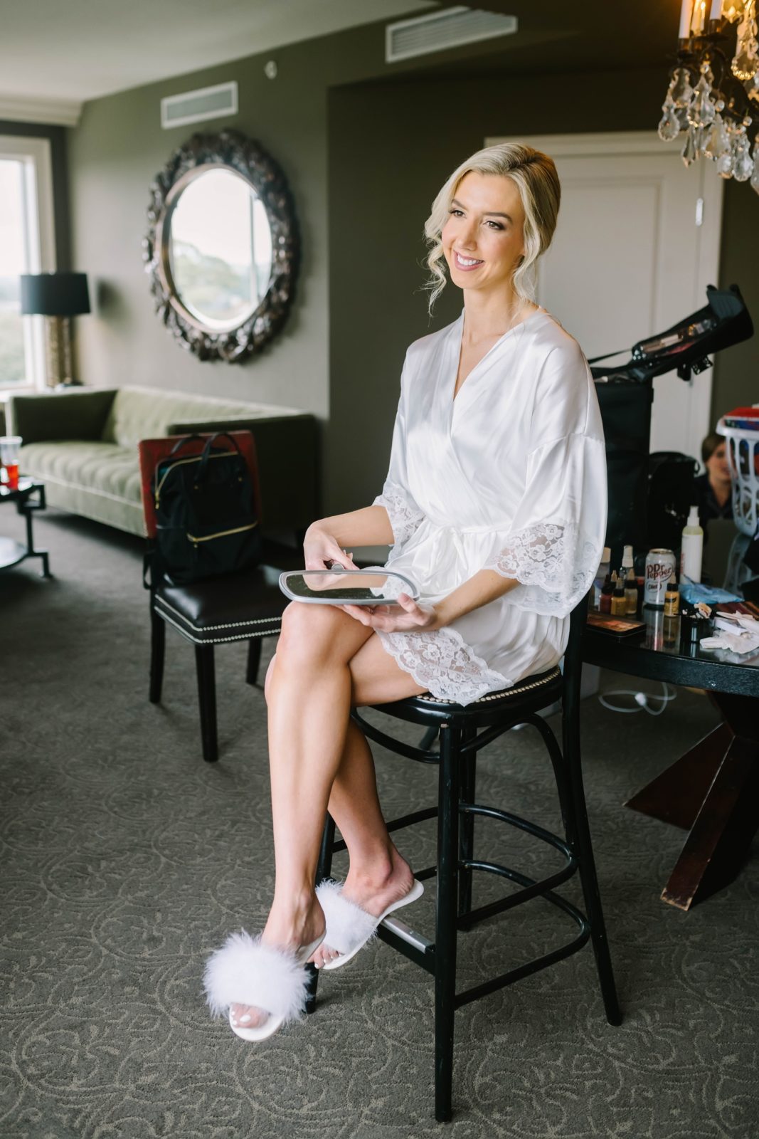 The bride sits on a stool in her white robe getting ready captured by Christina Elliott Photography. Bridal robe bridal makeup #christinaelliottphotography #Houstonweddings #catholicchurchweddings #navyblue #sayIdo #Houstonweddingphotographers