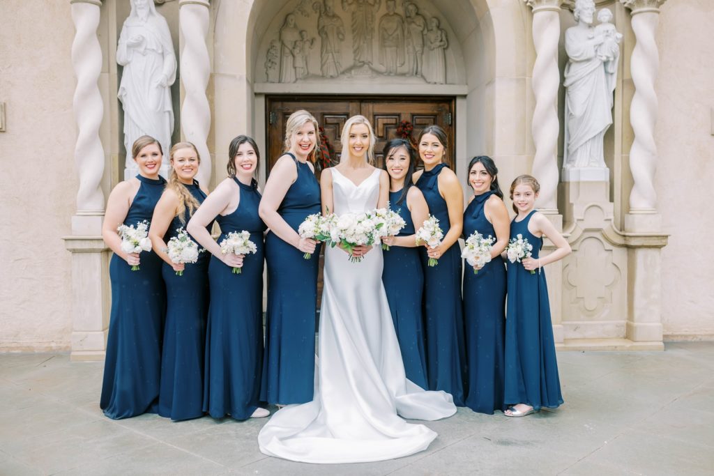 Bride poses with her eight bridesmaids in navy blue by Christina Elliott Photography. navy blue bridesmaid dresses bridal party #christinaelliottphotography #Houstonweddings #catholicchurchweddings #navyblue #sayIdo #Houstonweddingphotographers