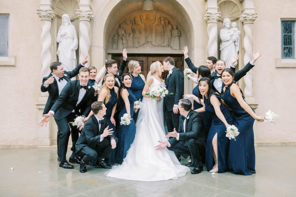 Christina Elliott Photography captures bridal party cheering as newlyweds kiss outside the chapel. church wedding classy weddings #christinaelliottphotography #Houstonweddings #catholicchurchweddings #navyblue #sayIdo #Houstonweddingphotographers