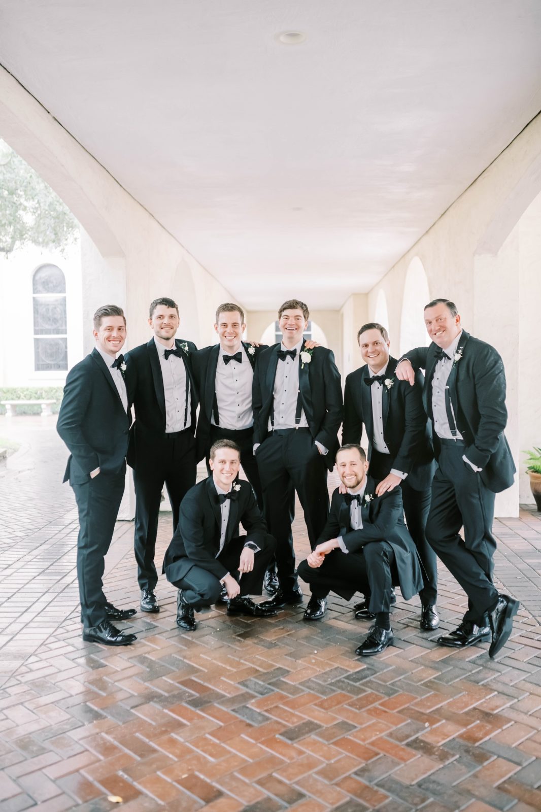 A group of groomsmen laughs while hugging one another captured by Christina Elliott Photography. groomsmen in black black bow ties #christinaelliottphotography #Houstonweddings #catholicchurchweddings #navyblue #sayIdo #Houstonweddingphotographers