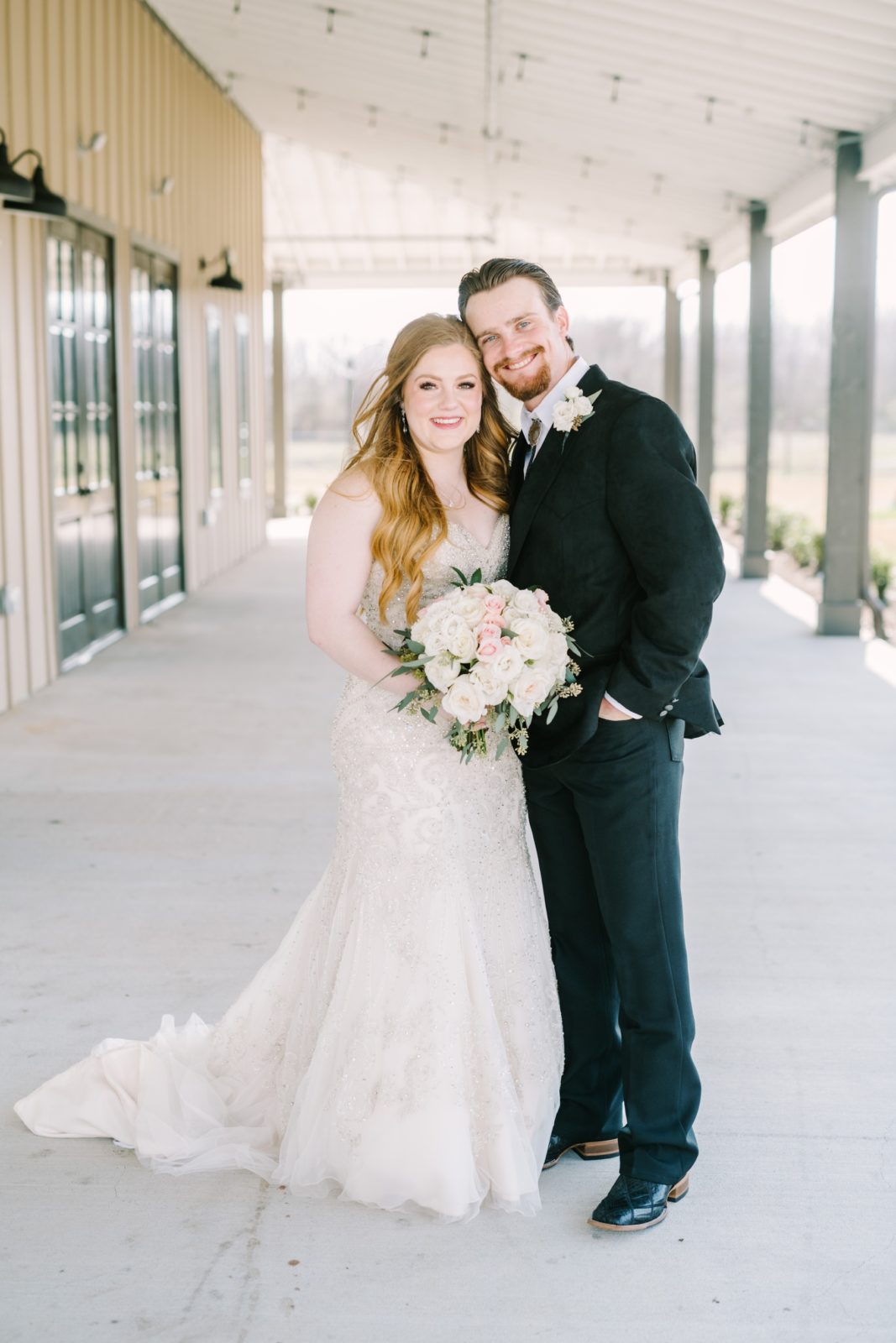 Portrait of a bride and groom next to a barn at Still Waters Ranch by Christina Elliott Photography. black suit barn wedding #ChristinaElliottPhotography #ChristinaElliottWeddings #StillWatersRanchWedding #Texasweddings #countrywedding #ranchwedding