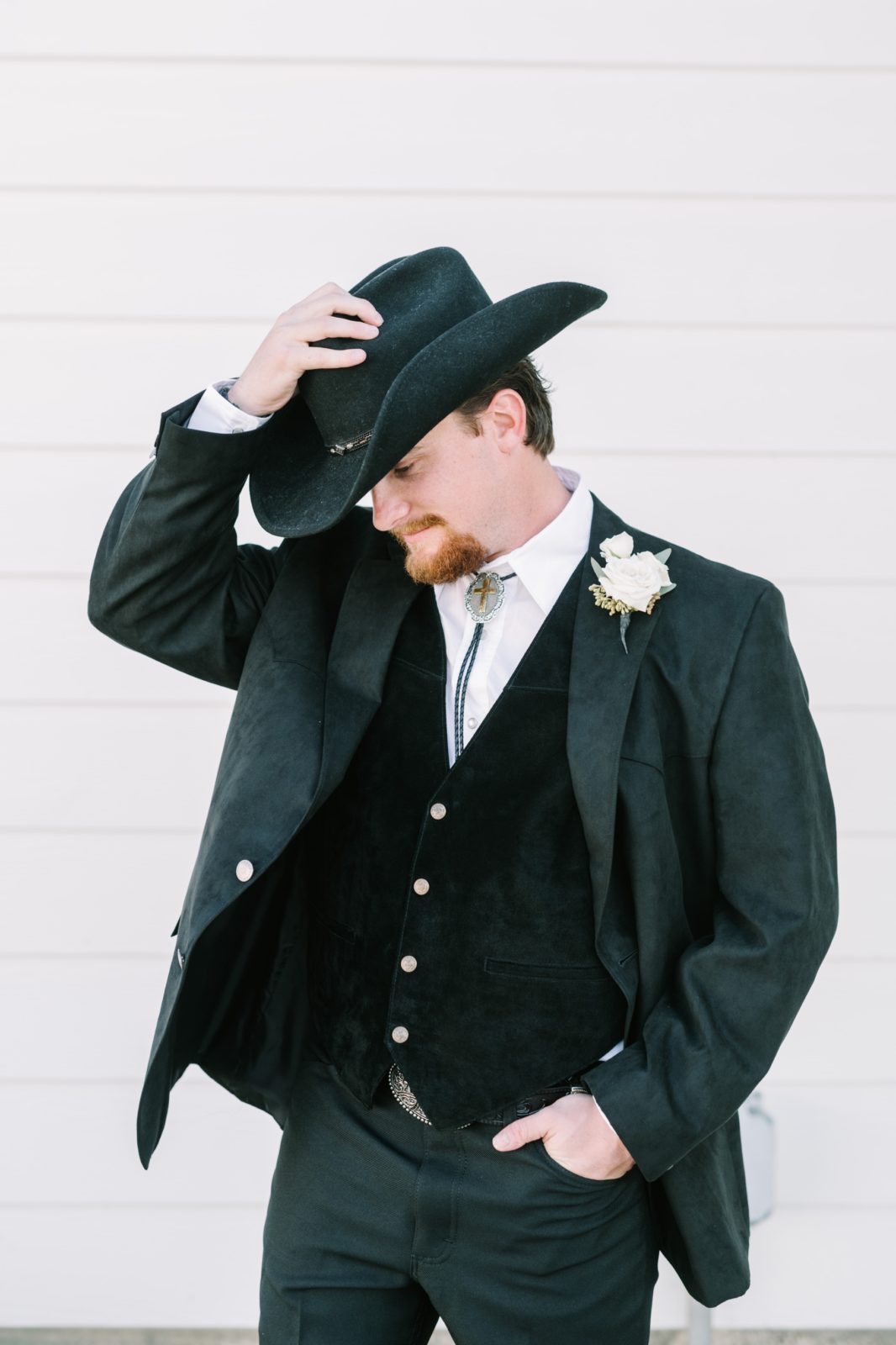 A groom with a cowboy hat tips his hat captured by Christina Elliott Photography. cowboy style for groom black vest #ChristinaElliottPhotography #ChristinaElliottWeddings #StillWatersRanchWedding #Texasweddings #countrywedding #ranchwedding