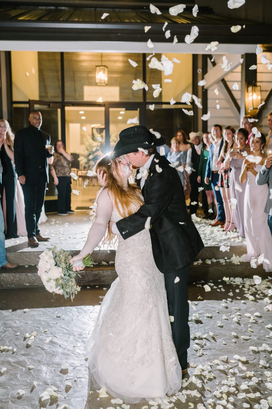 As petals are thrown in the air the bride and groom kiss captured by Christina Elliott Photography. wedding send-off #ChristinaElliottPhotography #ChristinaElliottWeddings #StillWatersRanchWedding #Texasweddings #countrywedding #ranchwedding