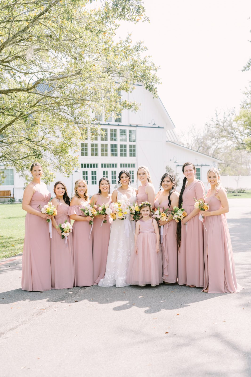 Outside a farmhouse, a bride smiles with her bridesmaids in East Houston by Christina Elliott Photography. pink bridesmaid dress #ChristinaElliottPhotography #ChristinaElliottWeddings #Houstonwedding #TheSpringsVenue #EastHoustonweddings #Mrs #Mr