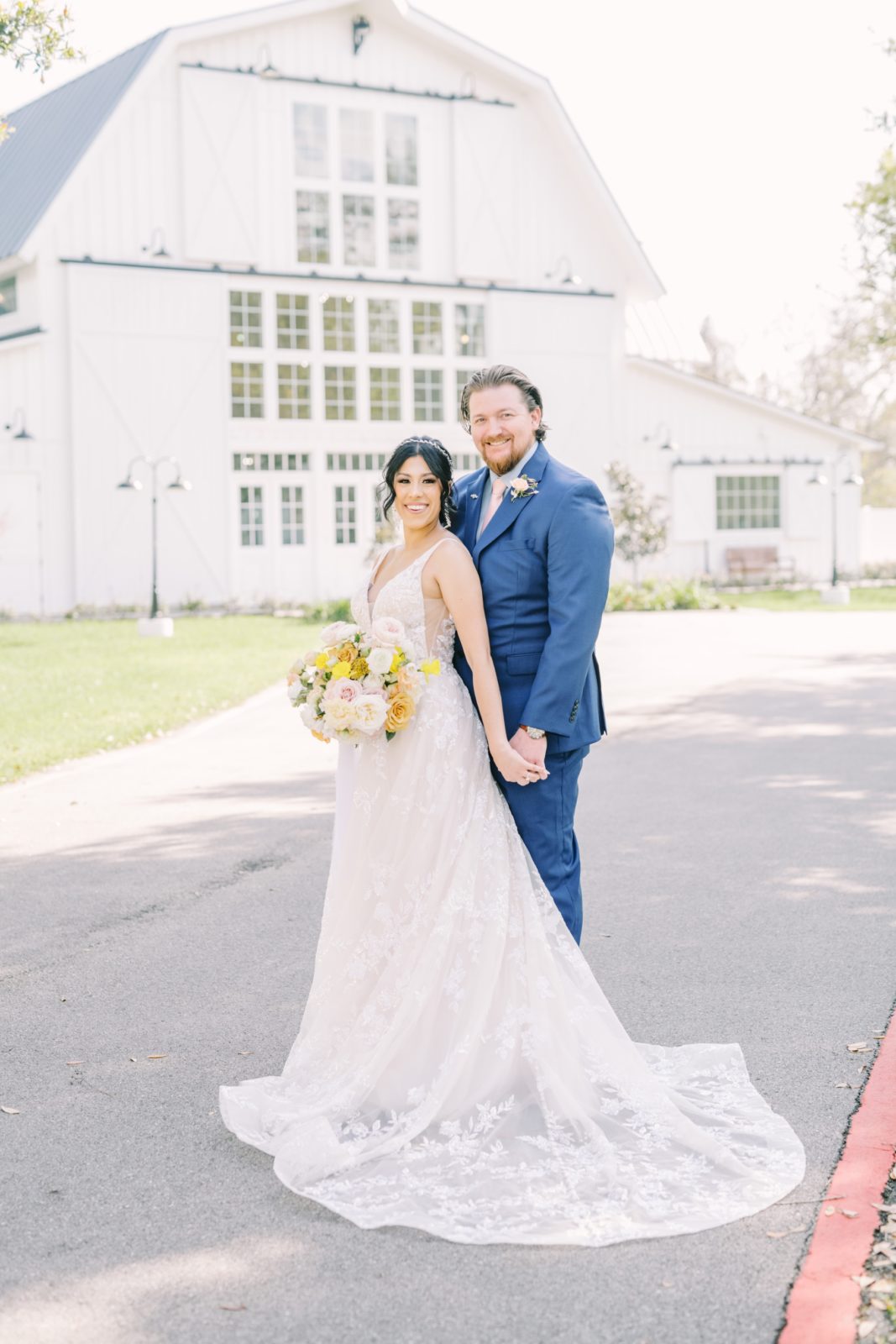 Holding hands a bride and groom smile in front of a southern barn on their wedding day by Christina Elliott Photography. blue suit #ChristinaElliottPhotography #ChristinaElliottWeddings #Houstonwedding #TheSpringsVenue #EastHoustonweddings #Mrs #Mr
