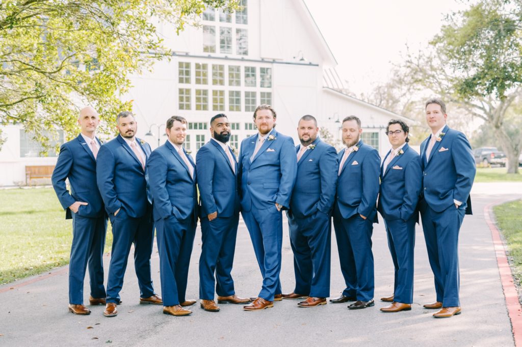 A groom with his groomsmen all wearing blue suits, brown shoes, and pink ties in Houston by Christina Elliott Photography. pink tie #ChristinaElliottPhotography #ChristinaElliottWeddings #Houstonwedding #TheSpringsVenue #EastHoustonweddings #Mrs #Mr